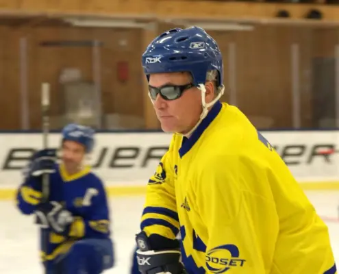 Blind Ice Hockey, man i gulblå hockeytröja, hjälm och mörka glasögon